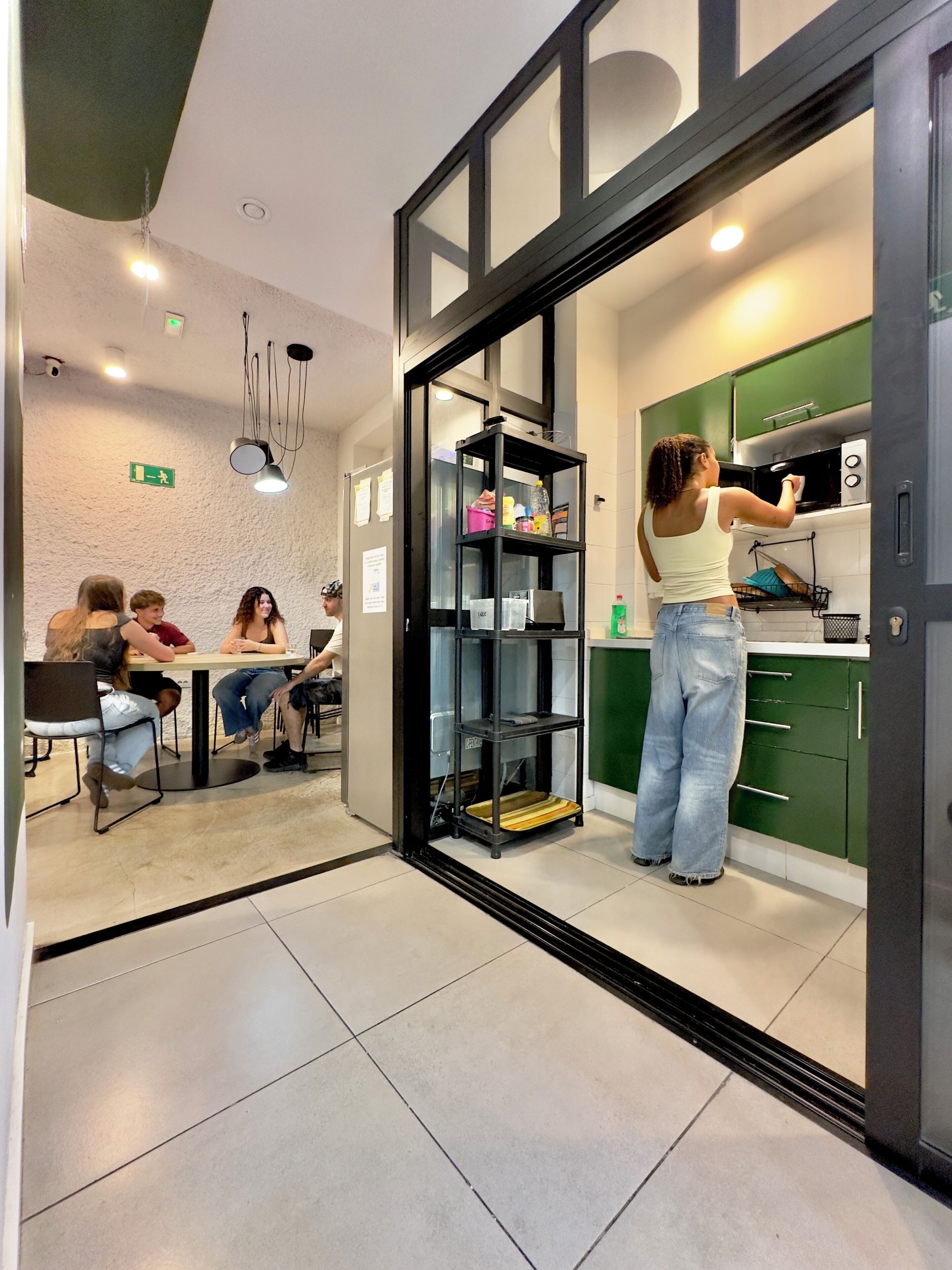 A modern interior with a dining area, a kitchen with green cabinets, and a person cleaning a microwave.