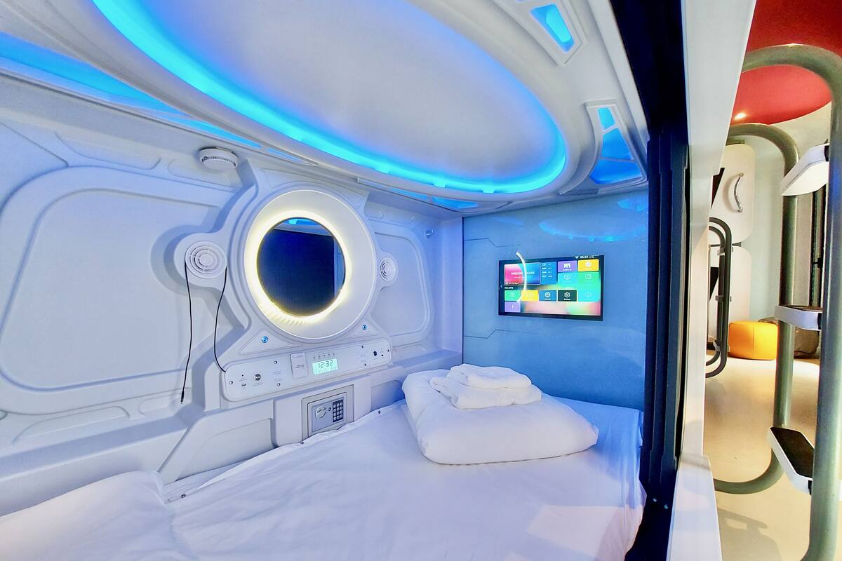 A modern, well-lit room with a circular window, a digital control panel, and a neatly made bed.