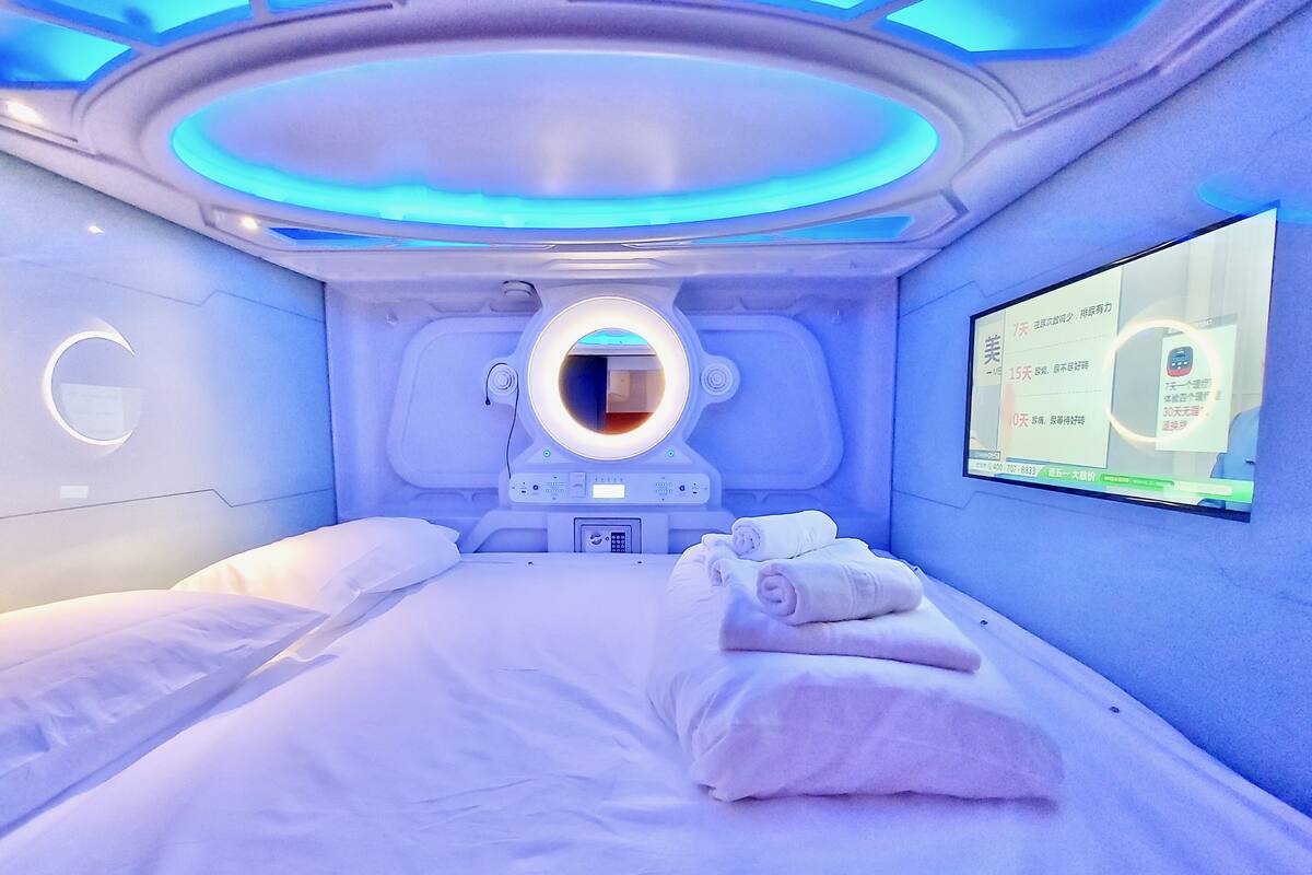 A modern room with a bed, a massage chair, and a digital display on the wall.