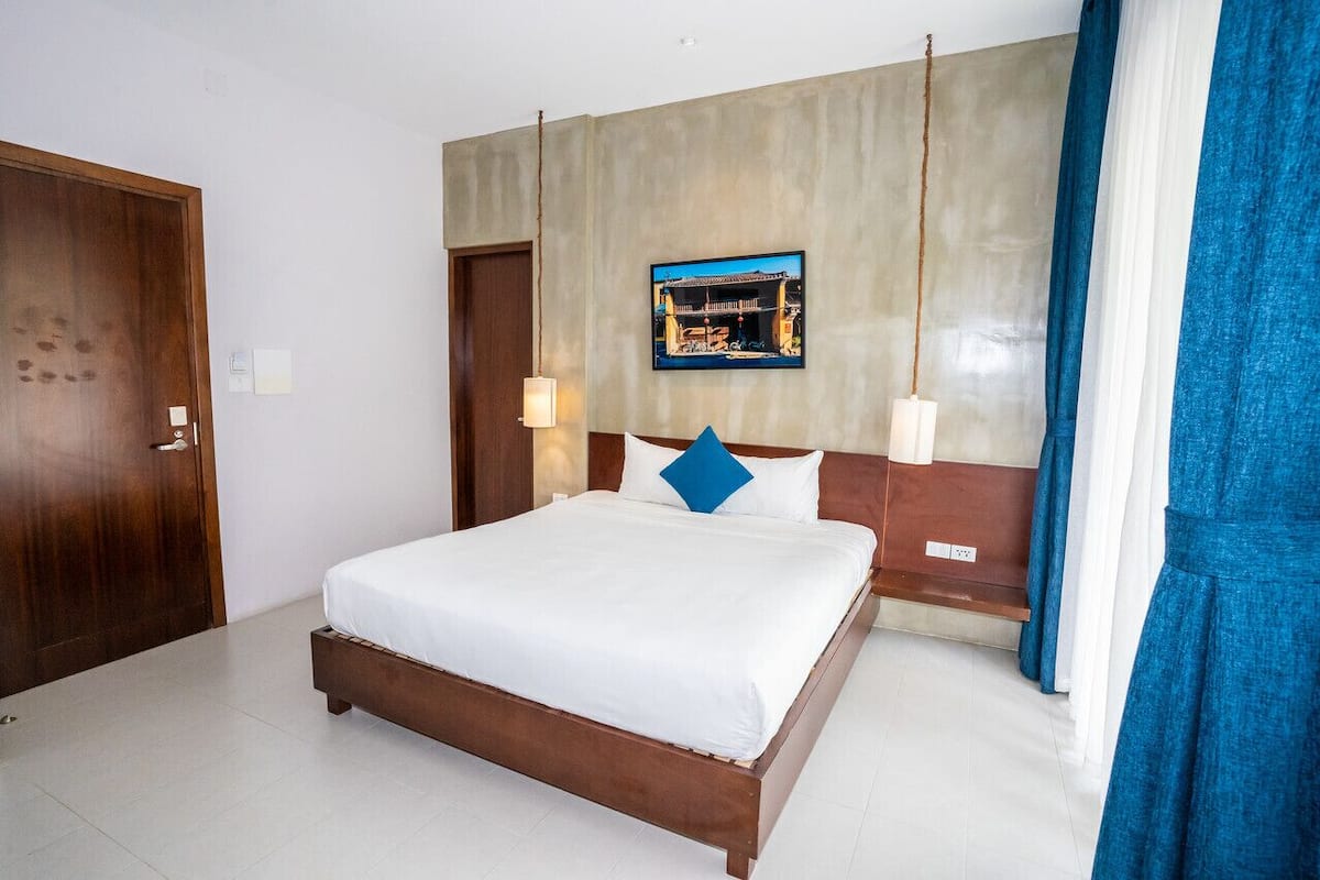 A hotel room with a wooden bed, a wall-mounted TV, and a large window with curtains.