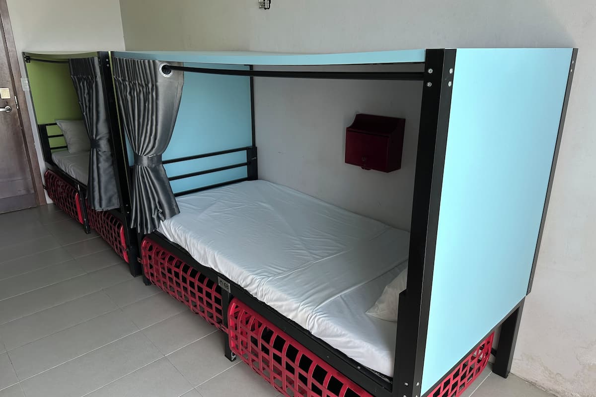 A single bed with a mosquito net, a red crate under the bed, and a small red box on the wall.