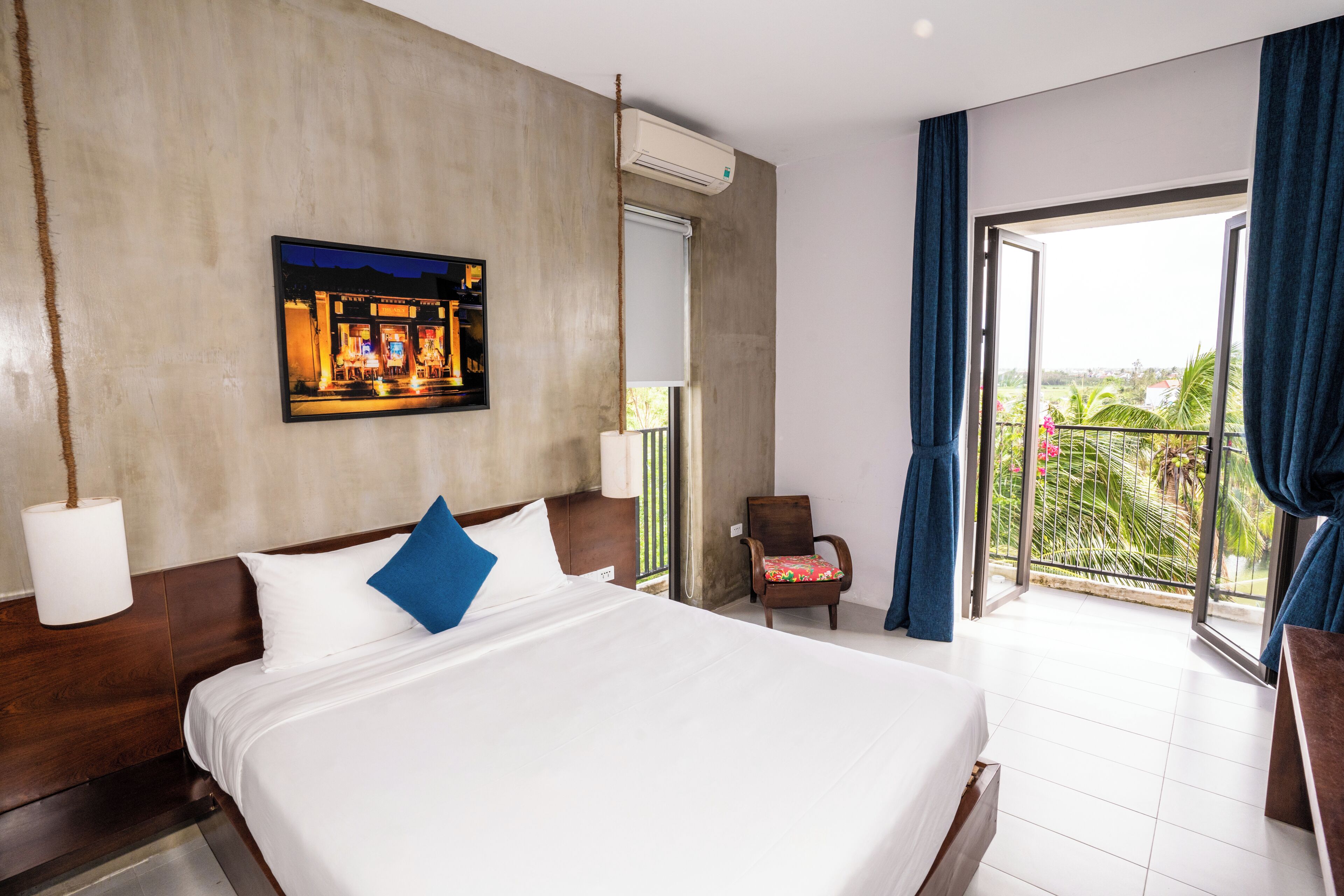 A hotel room with a large bed, a chair, a window with curtains, and a painting on the wall.