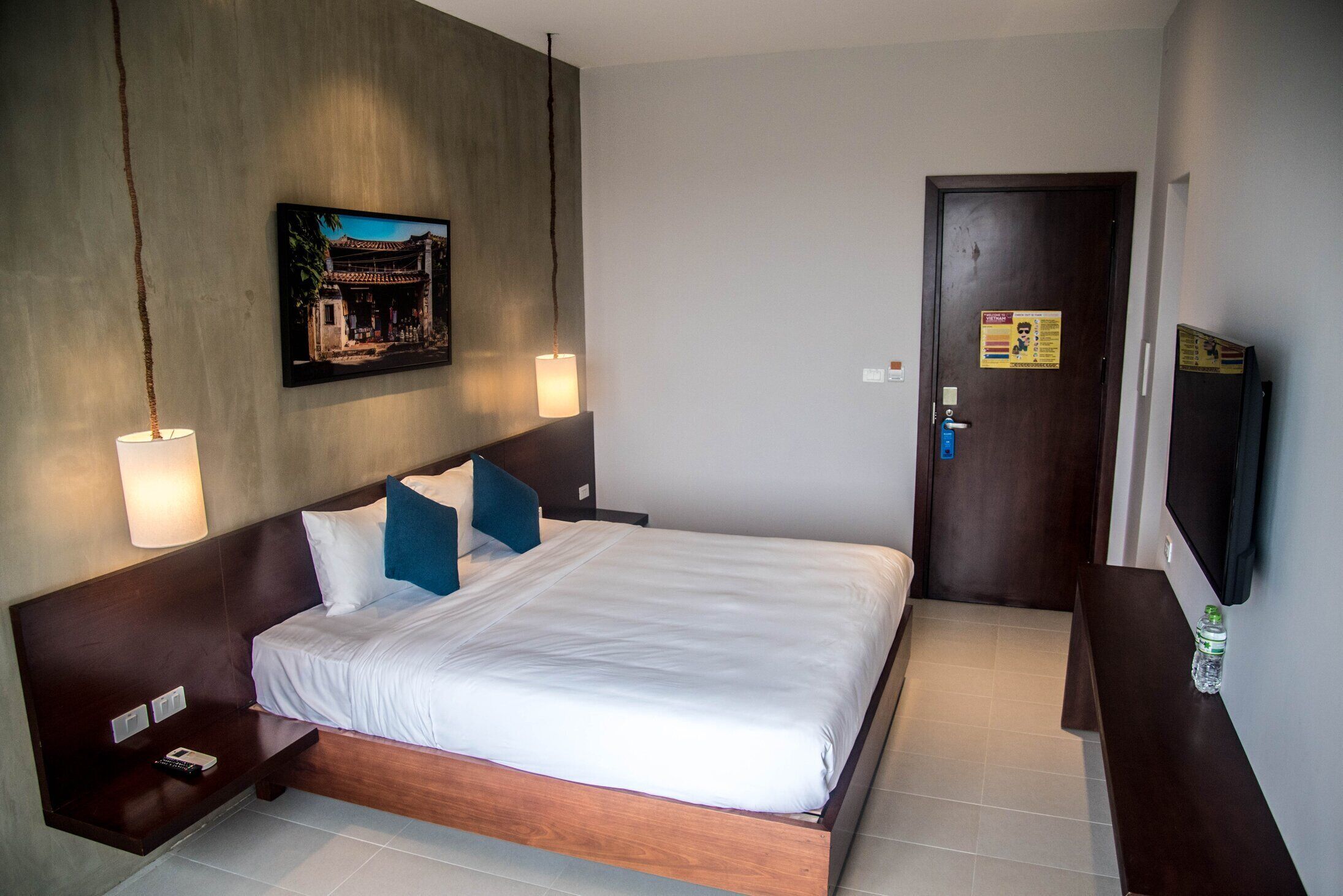 A hotel room with a large bed, a nightstand, a wall-mounted TV, and a painting above the bed.