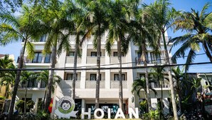 Un hotel con varios pisos, palmeras y un letrero con el nombre 'HOIAN'.