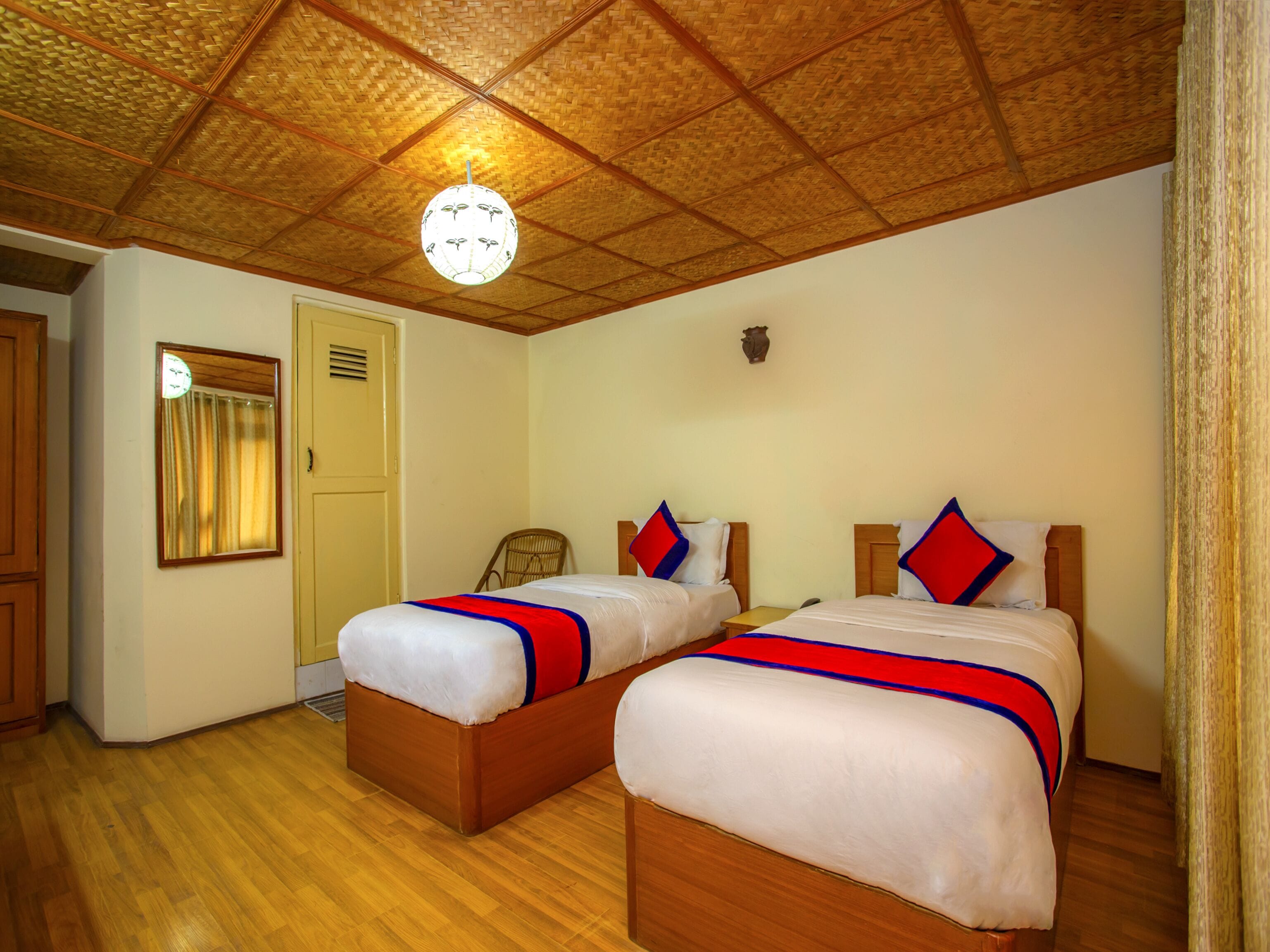 A room with two beds, wooden flooring, a woven ceiling, and a small table.