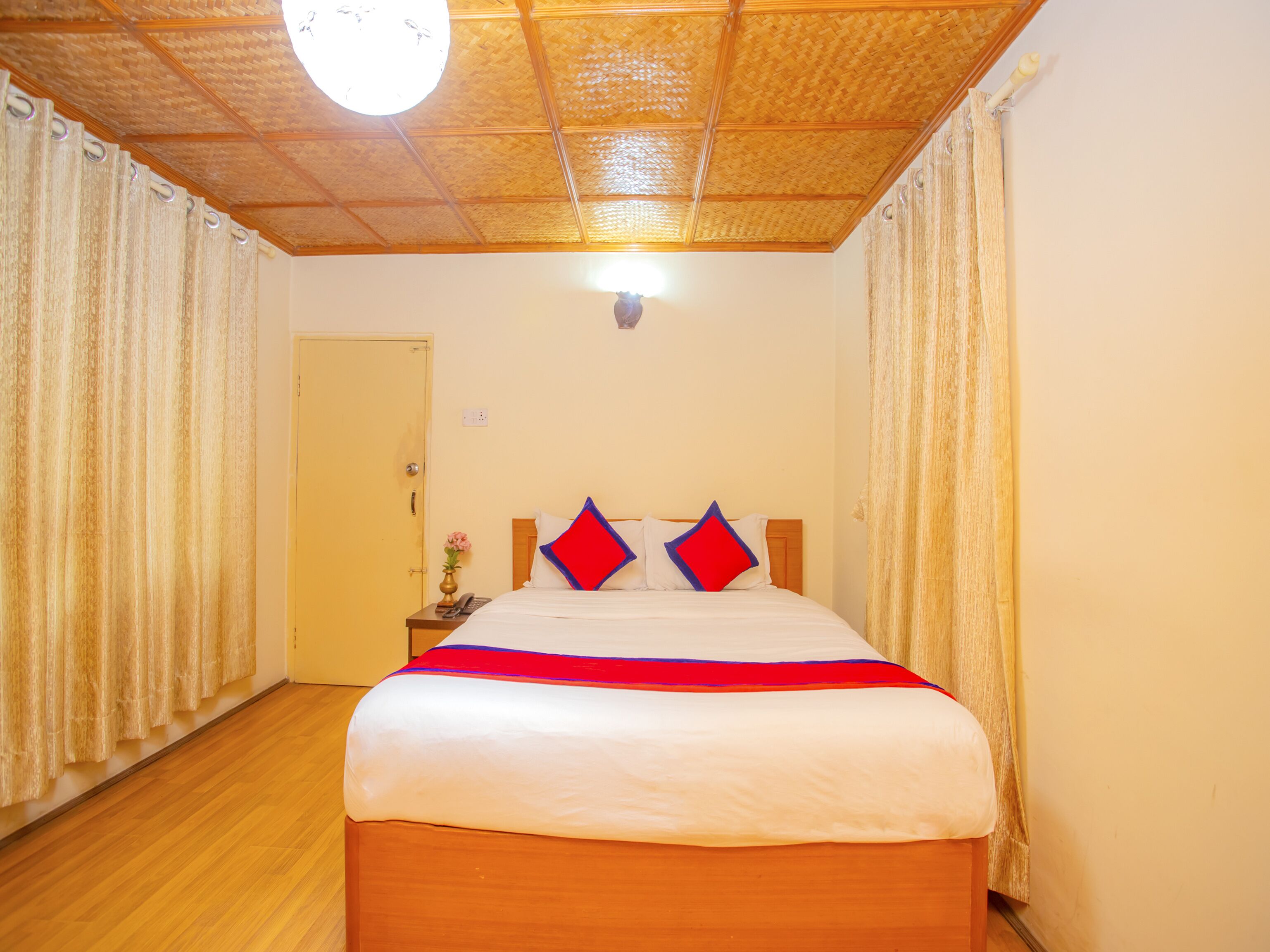 Una habitación de hotel con una cama de madera, una mesita de noche con un teléfono y un ventilador de techo.
