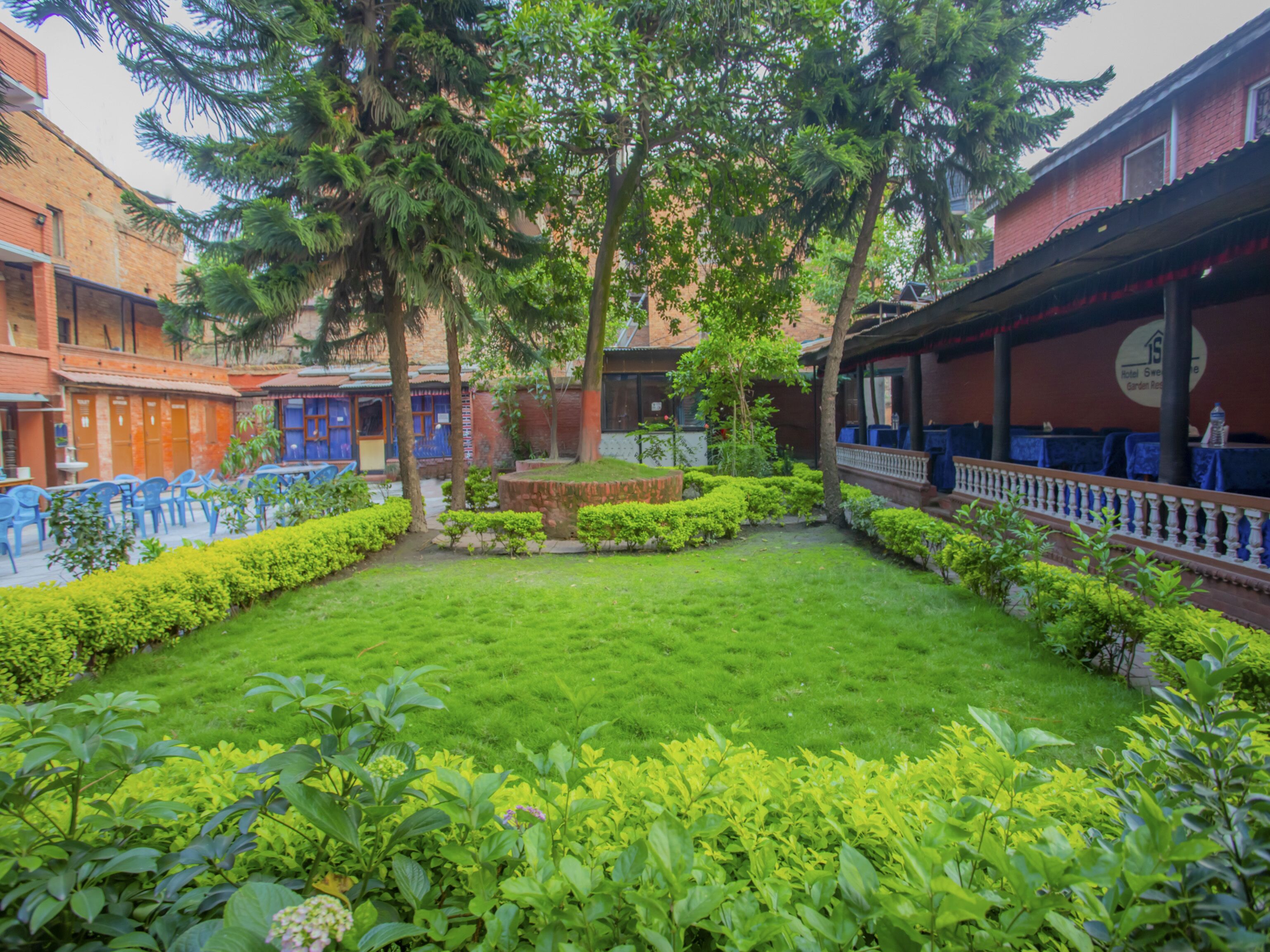 A courtyard with a well-maintained lawn, surrounded by buildings with brick facades and blue chairs.