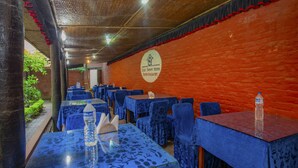 A restaurant with tables covered in blue tablecloths, a red brick wall, and a sign indicating it's a garden restaurant. - Sweet Home Hotel (Bhaktapur)