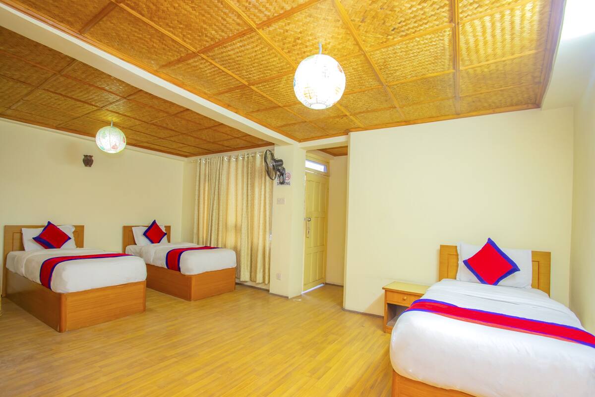 A hotel room with two single beds, a wooden floor, a ceiling fan, and a window with curtains.