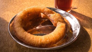 A plate with a ring-shaped food item and a glass of tea on a patterned tablecloth. - Sweet Home Hotel (Bhaktapur)