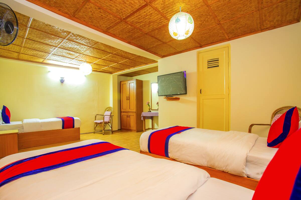A hotel room with two beds, a television, a wooden ceiling, and a small table with a vase.