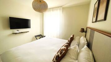 A hotel room with a bed, a mounted TV, and a hanging light fixture.