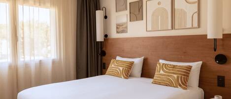A hotel room with a large bed, a nightstand, a lamp, and wall art.