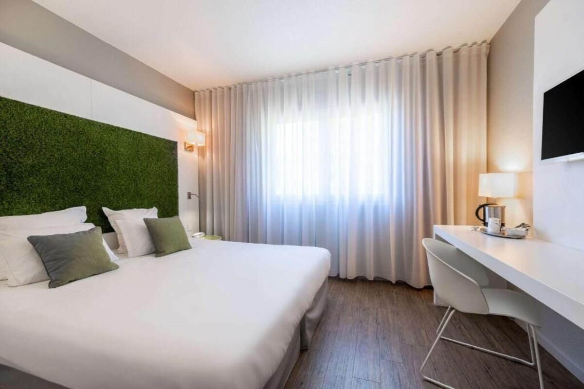 A hotel room with a bed, a desk, a TV, and a green wall.