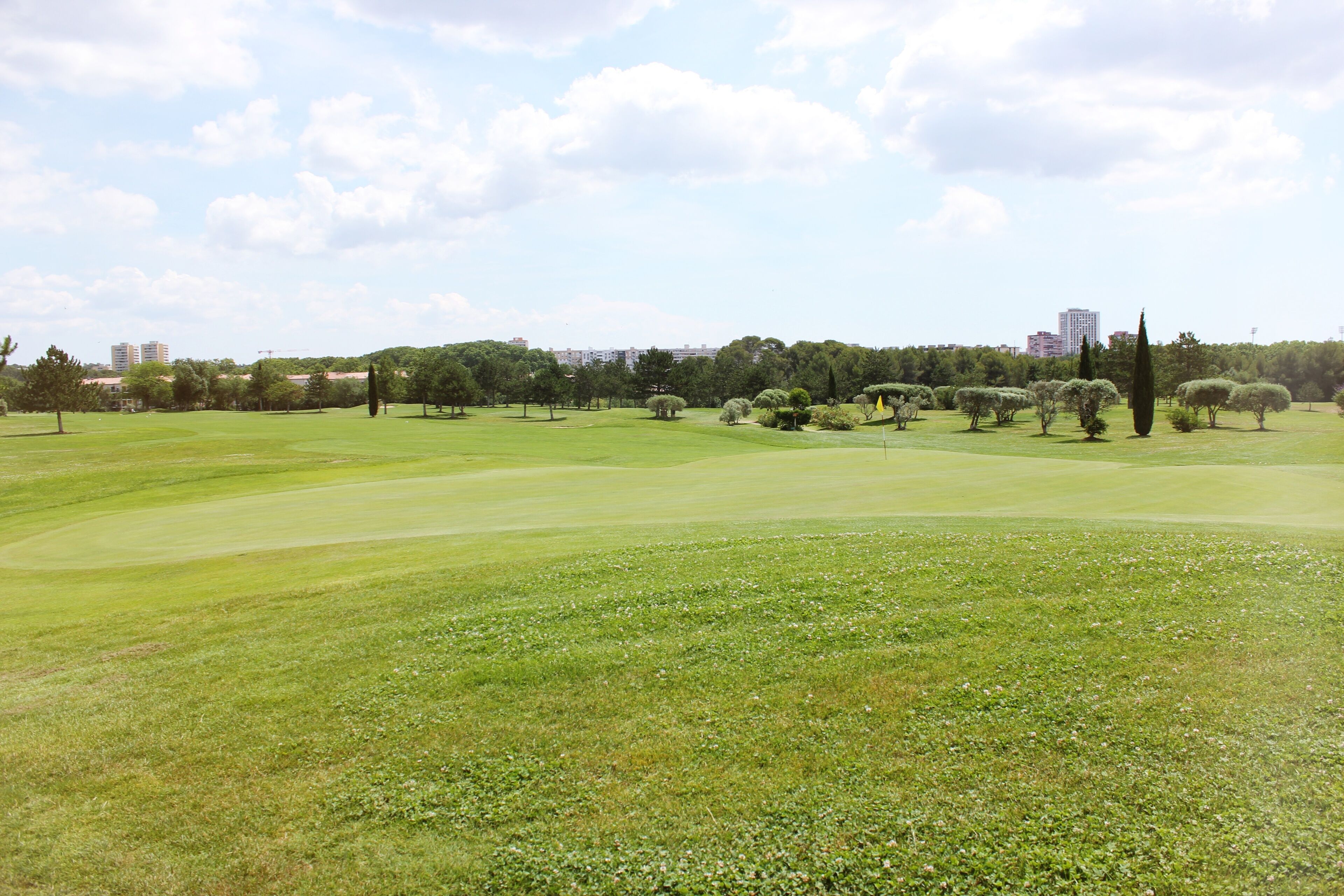 A golf course with a clear sky, trees, and distant buildings.