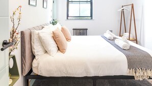 Un dormitorio moderno con cama, mesita de noche, lámpara colgante, ventana y radiador.