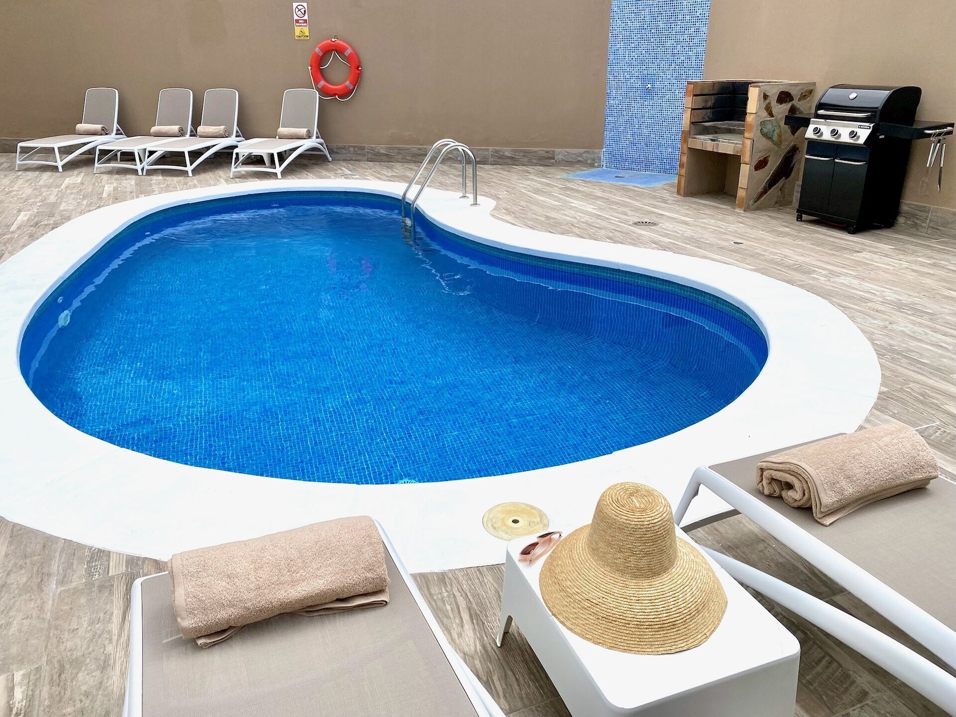 A swimming pool with lounge chairs and a barbecue area.