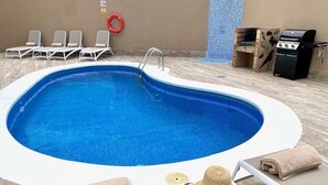 Una piscina con sillas de descanso y zona de barbacoa.