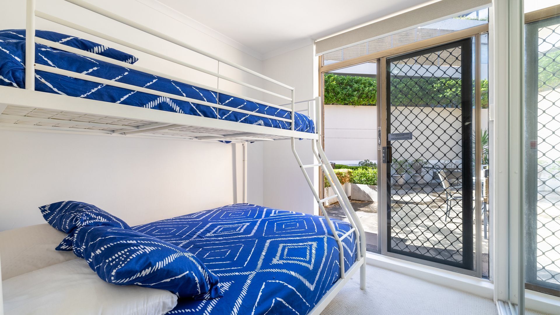 Camera con letto a castello e vista su un giardino attraverso una porta di vetro.