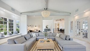 Ein geräumiges Wohnzimmer mit einem großen, grauen, L-förmigen Ecksofa, einem Holztisch und einem gemusterten Teppich.