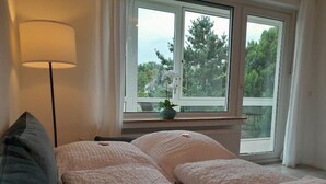 A bedroom with two beds, a window with a view of trees, a floor lamp, and a small plant on the windowsill. - 4-room vacation apartment - renovated - WLAN - Netflix (Castrop-Rauxel)