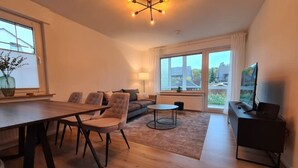 A modern living room with a dining area, large windows, and a TV. - 4-room vacation apartment - renovated - WLAN - Netflix (Castrop-Rauxel)