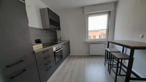 A compact kitchen with a built-in oven, a microwave, and a small dining area with a table and two stools. - 4-room vacation apartment - renovated - WLAN - Netflix (Castrop-Rauxel)