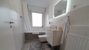 A small, modern bathroom with a toilet, sink, and shower. - 4-room vacation apartment - renovated - WLAN - Netflix (Castrop-Rauxel)