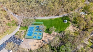 Eine Vogelperspektive auf einen Tennisplatz, umgeben von Bäumen, einem Parkplatz und einem kleinen Gebäude.