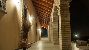 Un corredor al aire libre cubierto, con pilares de piedra y suelo de baldosas, que conduce a la entrada de un edificio.