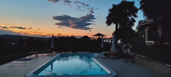 Relax by the pool surrounded by lounge chairs and umbrellas, with a gazebo offering shade nearby.
