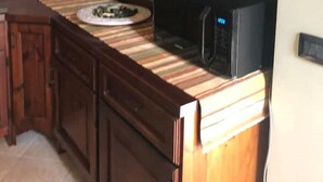 Una cocina con armarios de madera, encimera a rayas y estantes con platos y un microondas.