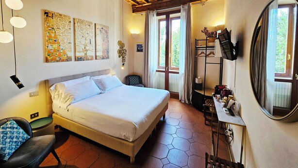 A bedroom with a bed, a chair, a desk with a mirror, and artwork on the walls. - SPIRIT OF FLORENCE Boutique Rooms (Florence)