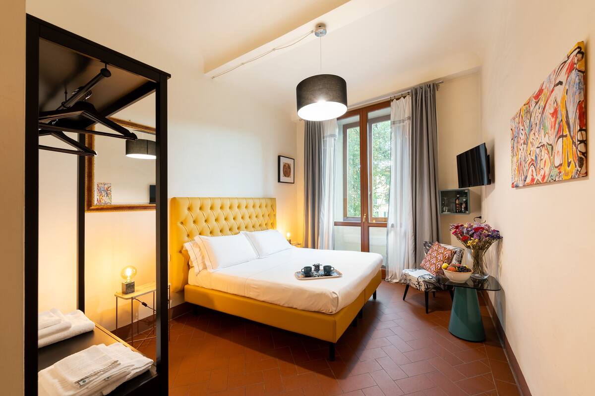 A hotel room with a large bed, a mirror, a television, and a window with curtains.