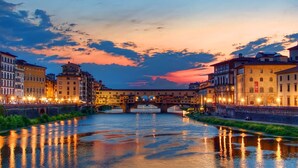 A river with buildings on either side, a bridge in the middle, and a sunset sky. - SPIRIT OF FLORENCE Boutique Rooms (Florence)