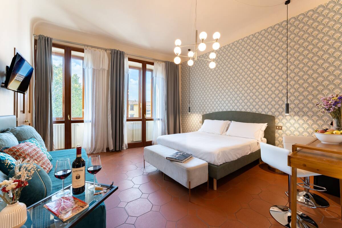 A modern hotel room with a large bed, a sofa, a dining table, and a TV.