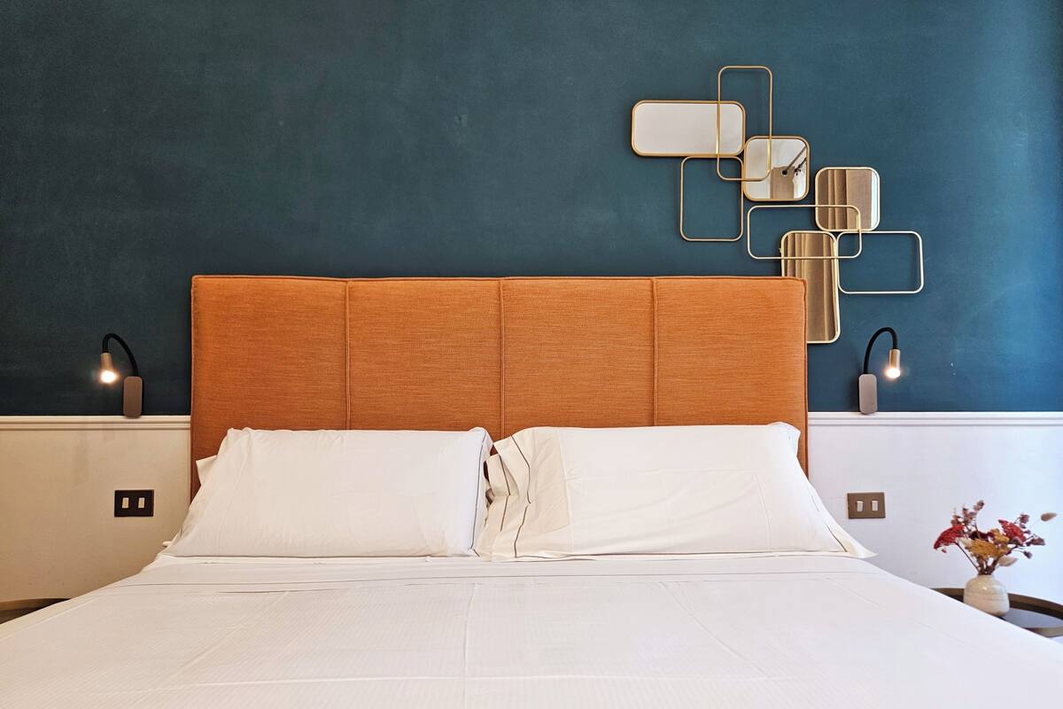 A neatly made bed with white linens, a wooden headboard, and a wall-mounted light fixture.