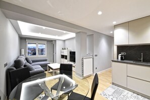 Una sala de estar moderna con una mesa de comedor de vidrio, un sofá gris y vistas de la ciudad a través de amplias ventanas.