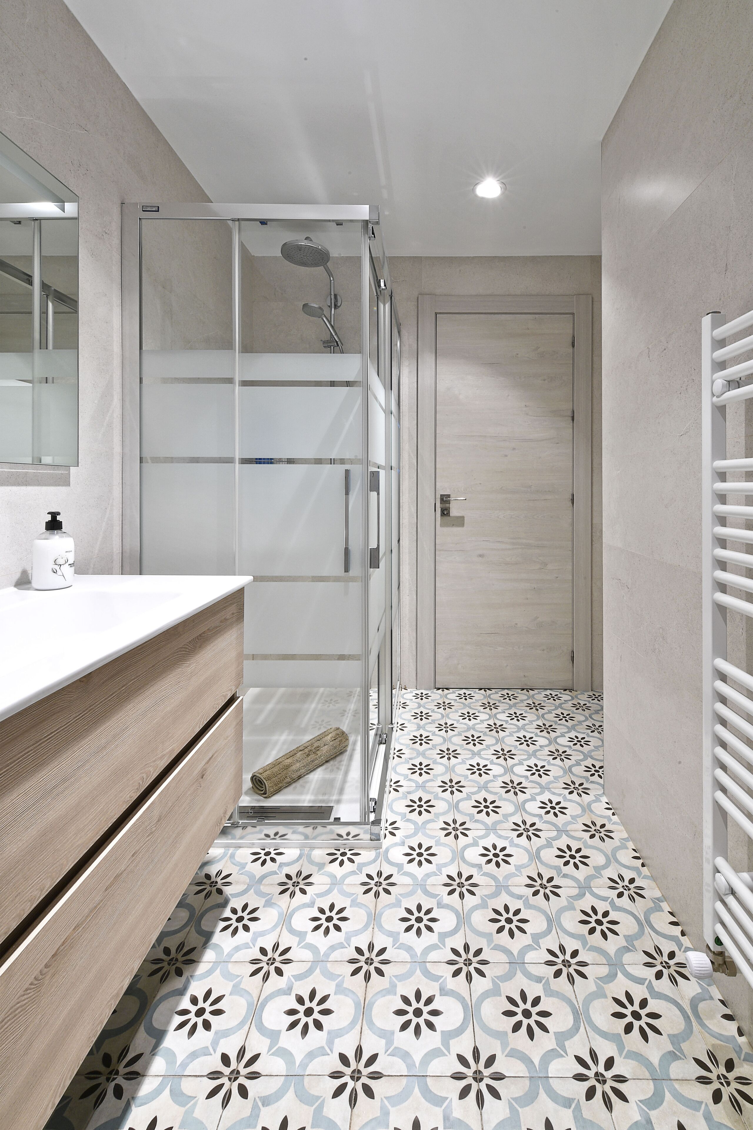 Een moderne badkamer met een douchecabine van glas, een houten wastafelmeubel en vloertegels met een patroon.