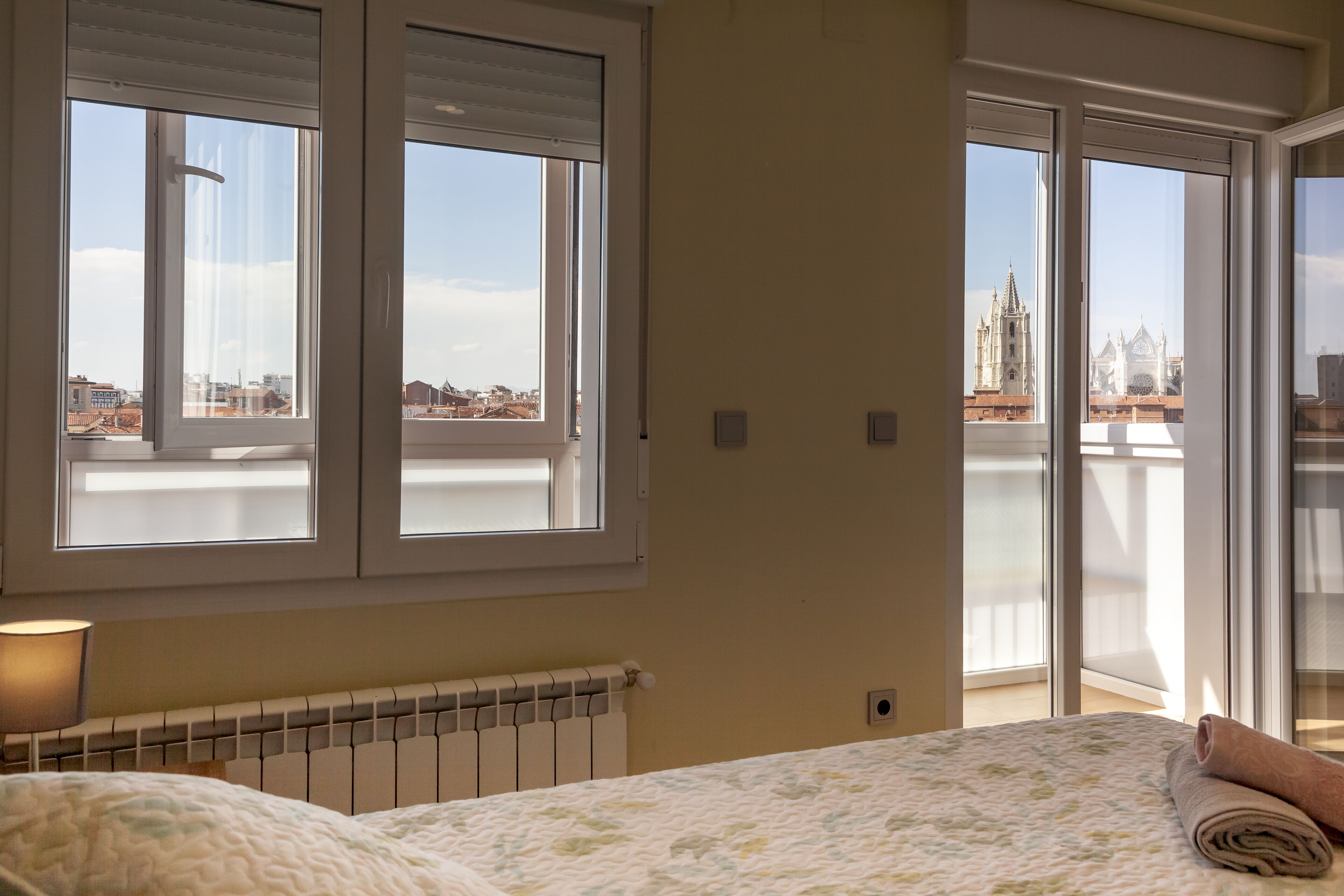 Un dormitorio con cama, un radiador y una ventana con vistas a edificios y una iglesia.