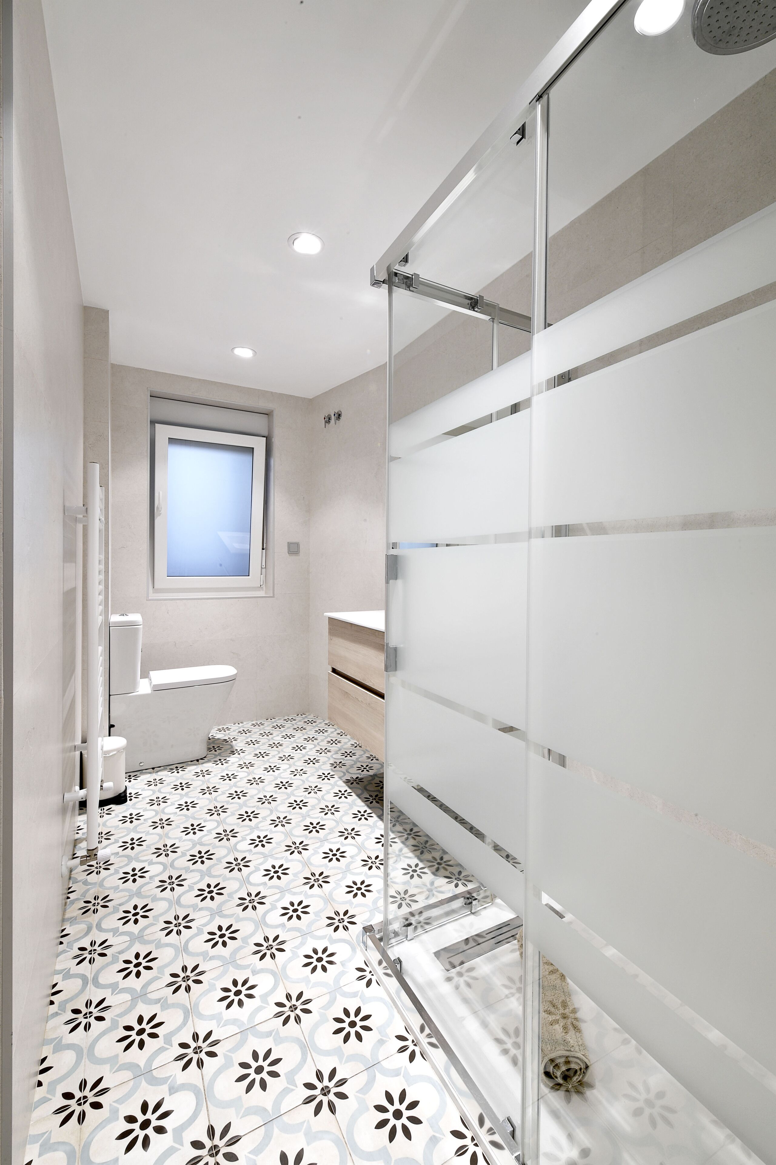A modern bathroom with a patterned floor, a window, and a glass shower enclosure.