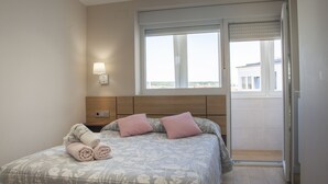 A bedroom with a bed, a nightstand, a wall-mounted lamp, and a window with a view.