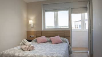 Un dormitorio con cama, mesita de noche, lámpara de pared y ventana con vistas.