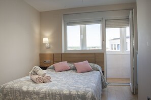Un dormitorio con cama, mesita de noche, lámpara de pared y ventana con vistas.