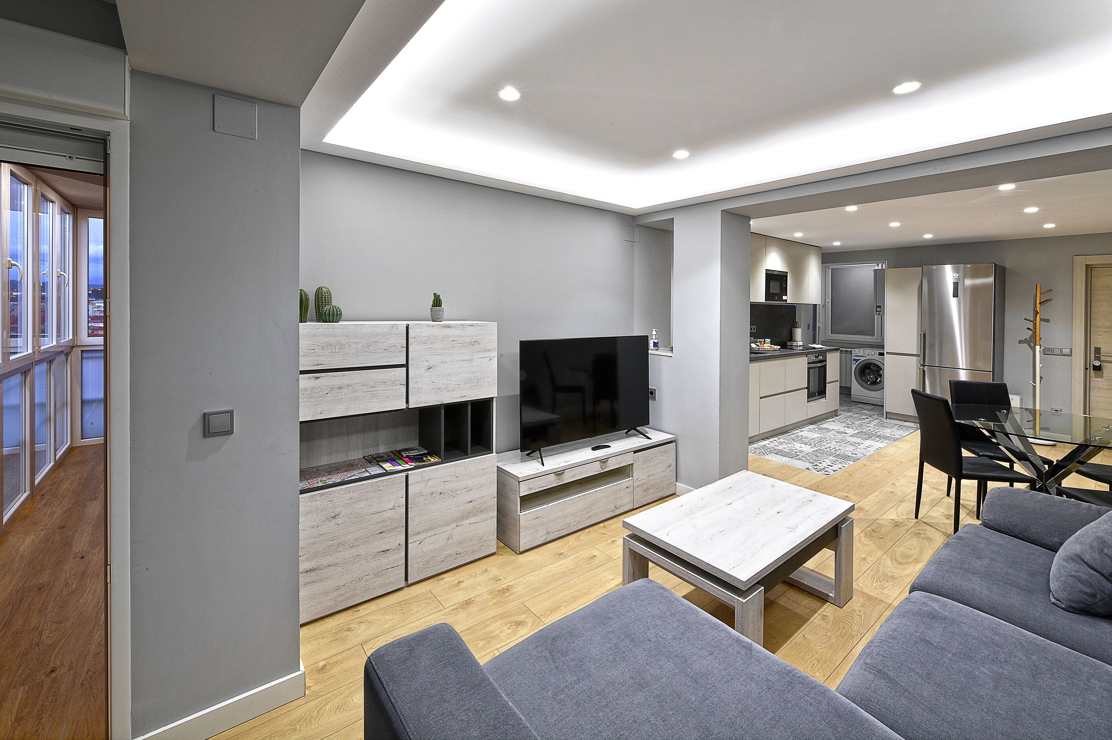 Una sala de estar moderna con un televisor de pantalla plana, sofás grises y un comedor con mesa de vidrio.