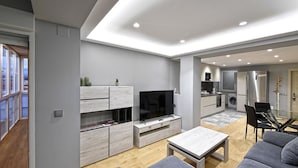 A modern living room with a flat-screen TV, grey sofas, and a dining area with a glass table.