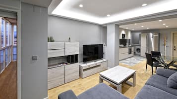 Una sala de estar moderna con un televisor de pantalla plana, sofás grises y un comedor con mesa de vidrio.