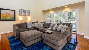 A living room with a sectional sofa, two side tables, a rug, and a large window with a view. - Spacious Mt. Bachelor Retreat w/ Hot Tub + Pets OK (Bend)