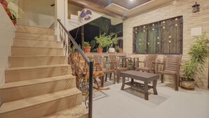 Uma escadaria que dá acesso a um segundo andar, uma área de jantar com cadeiras e uma mesa, e uma janela com grades decorativas.