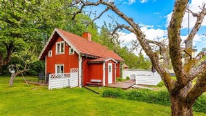 Una casa in legno rossa con tetto spiovente, un cortile recintato e un grande albero in primo piano.
